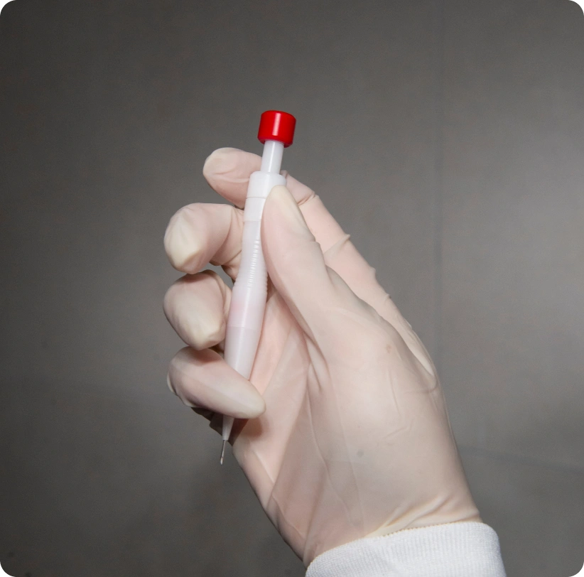 Ruka v bílé ochranné rukavici drží aplikátor pro transplantaci vlasů